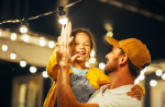 A father holding a little girl while she is helping fix a string light