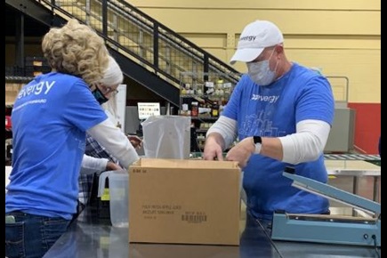 Two Evergy volunteers in blue shirts pack a box of food items for distribution