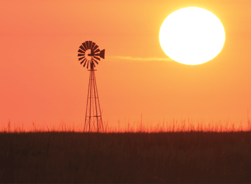 A hot sun going down in Kansas near a windmill